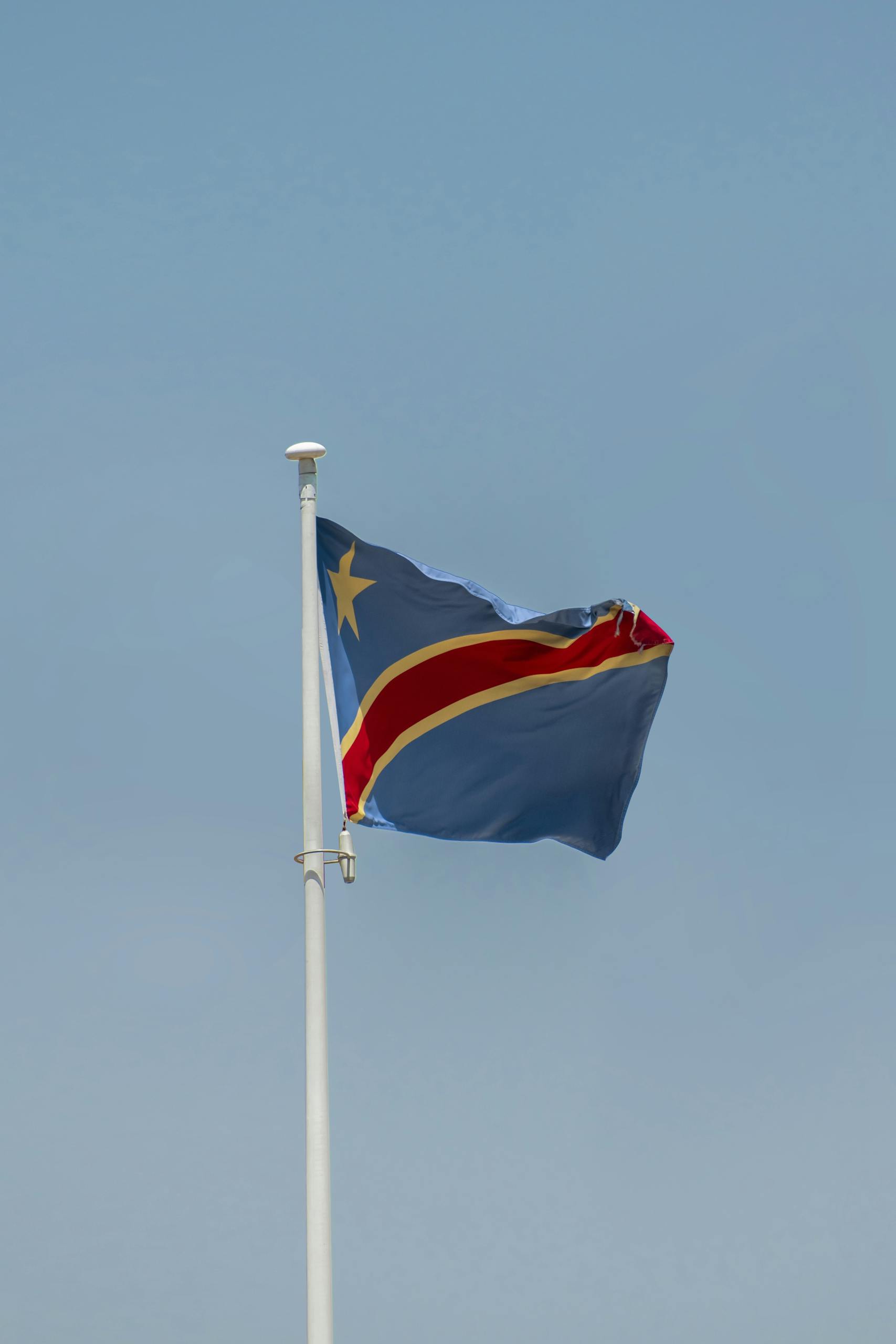 Waving flag of the Democratic Republic of the Congo under a clear blue sky.